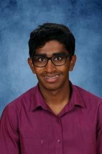 Young man smiling in purple shirt with glasses.